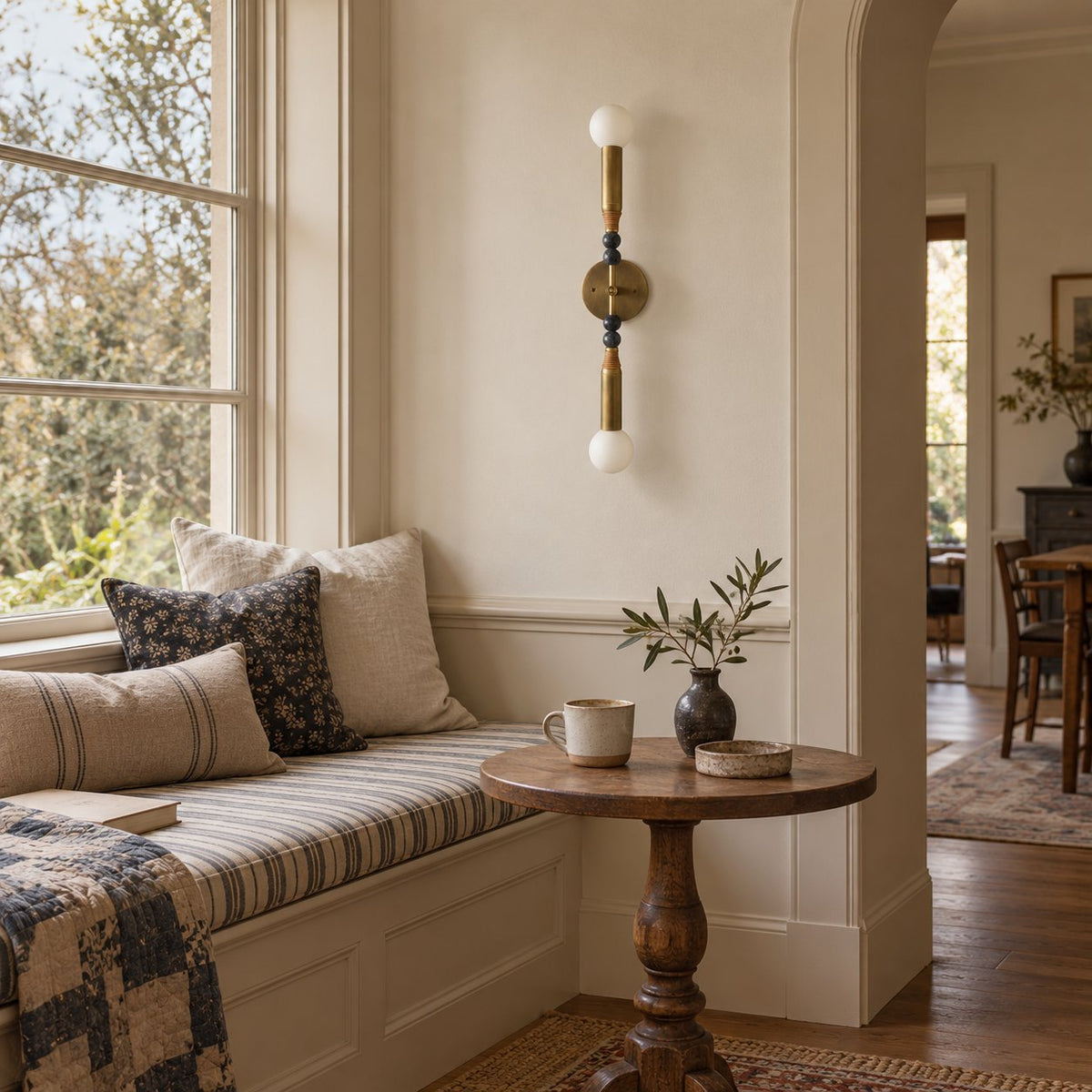 Torto wall sconce in antique brass with marble bead accents and glass globes above a window seat.