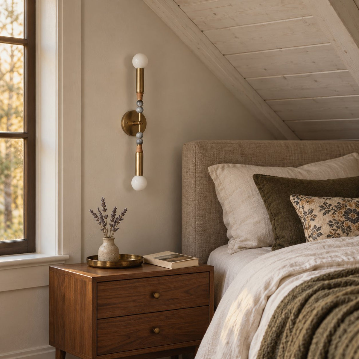 Torto wall sconce in antique brass with marble bead accents and glass globes above a bedroom nightstand.