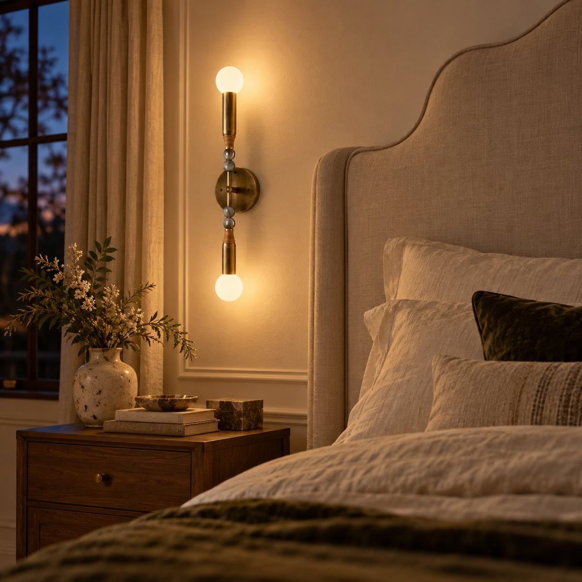 Torto wall sconce with a brass stem, marble beads, and glass globes beside a bed.