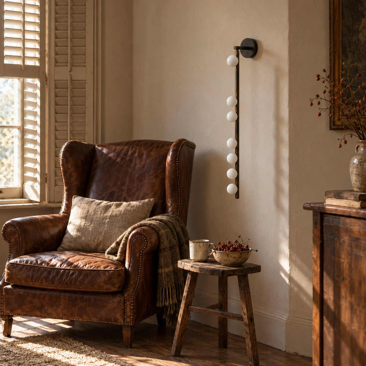 Vouga bronze vertical bar sconce with small white glass globes beside a leather armchair.