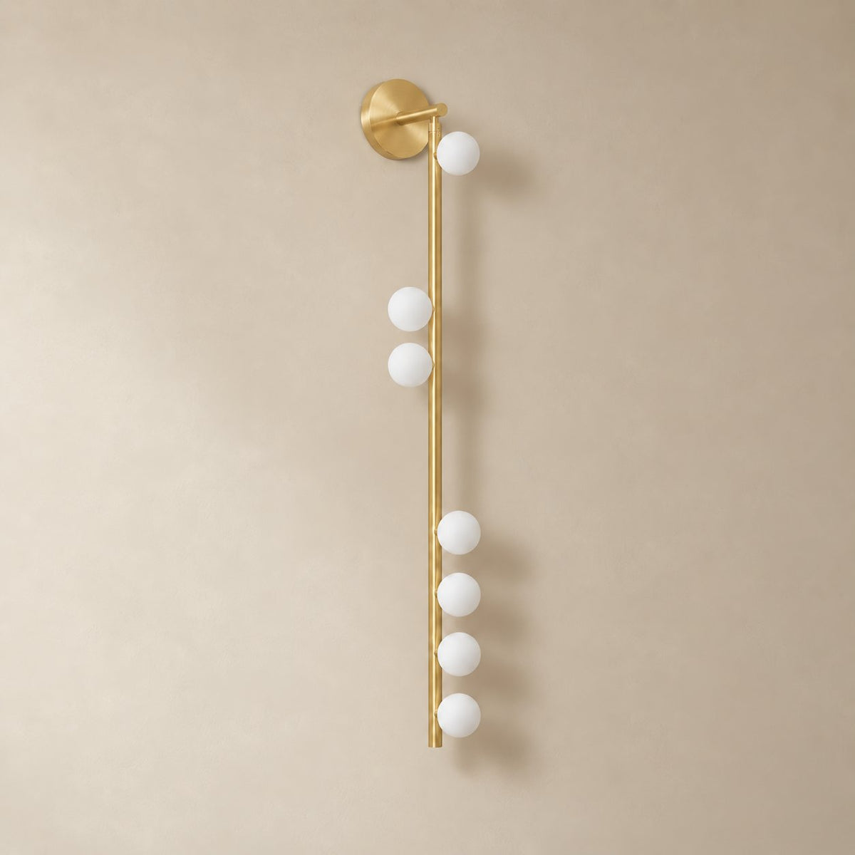 Vouga glass tube wall sconce in brushed brass, 7 heads A, 100 cm, unlit on a plain plaster wall.