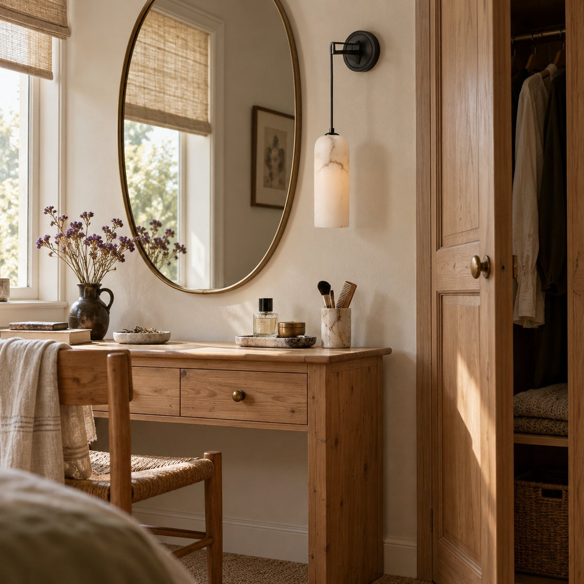 Zêzere black wall sconce with an alabaster shade beside an oval mirror above a wood dressing table.