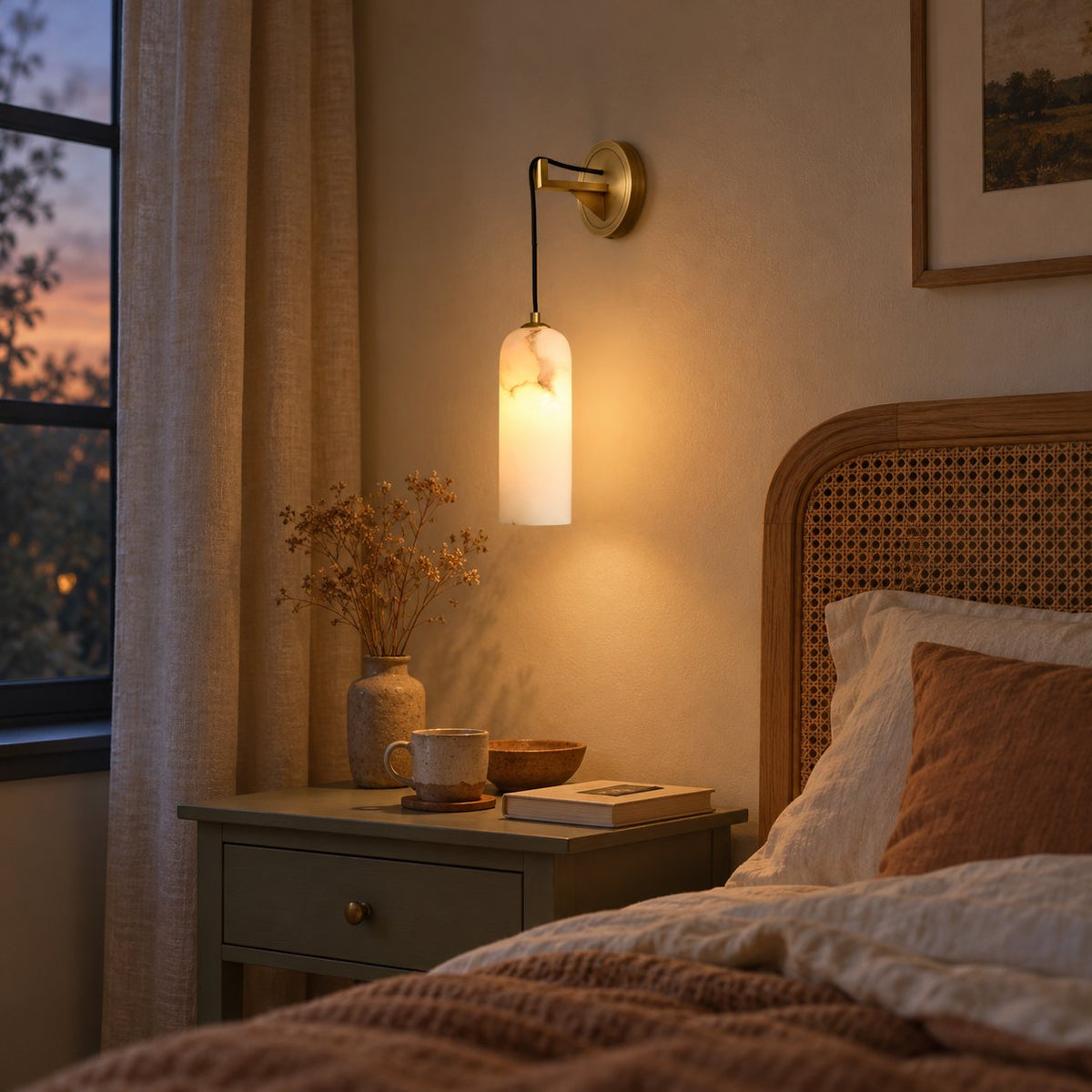 Zêzere brass wall sconce with a marbled alabaster cylinder shade above a cane headboard bed at dusk.