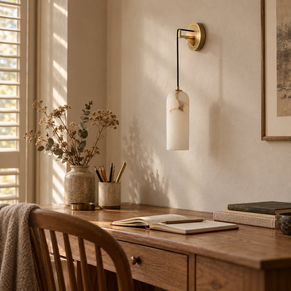 Zêzere alabaster wall sconce on a brass arm above a wooden writing desk.